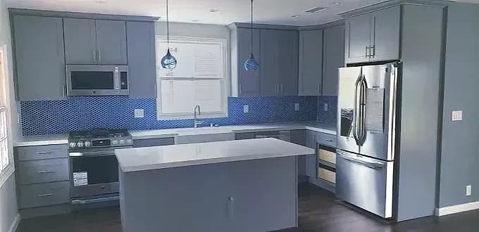 Modern kitchen remodel in Beaverton OR with slab-front gray cabinets, white quartz island, iridescent blue glass backsplash, and blue blown-glass pendants